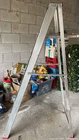 Side view of 6ft aluminum stepladder showing full profile and storage items in garage background.