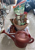 Photo of grass seed, turf builder tool, plant pot, watering can, and soil bags arranged on garage floor.