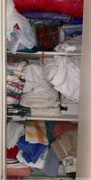 Closet shelves with folded assorted white, purple, and patterned bedding and linens stacked