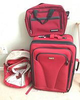 Three red bags including a Jetliner carry bag on top of a large Jetliner luggage suitcase with a Canadian Olympic Team backpack beside.