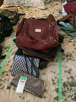 Stack of purses featuring a brown croc-embossed leather shoulder bag, a small black purse with silver beaded pattern, and a brown snakeskin purse with tag attached