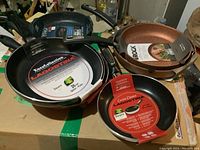 Overview of multiple frying pans including Lagostina and The Rock, all with original packaging