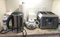 Countertop photo showing all five items: Cuisinart toaster, Breville electric kettle, floral teapot, kitchen scale, and London cookie jar arranged from right to left.