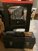 Photo showing black plastic toolbox and sawhorse with red top, three hand files on top of toolbox.