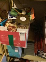 Photo of a box with electrical items including a white porcelain lampholder, boxed socket set, and hand broom in background on a shelf