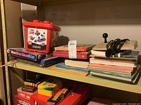 Shelf with red Classic Lego container, assorted children's books, and boxes of games and puzzles.