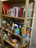 Three-shelf unit with assorted cleaning supplies, hair care products, and other household items including boxed lightbulbs.