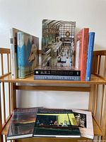 Photo of 10 hardcover museum collection books arranged on wooden shelves showing titles and cover images related to art and museums.