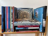 Photo showing a total of 16 architecture books stacked on a wooden shelf, titles visibly including 'Contemporary Spanish Architects', 'Venetian Villas', 'Inside Architecture', and others.