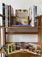 Photo of 14 gardening books arranged on a wooden shelf including encyclopedia of herbs and vegetable magazines
