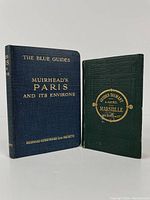 Two hardcover vintage travel guides; one blue (Muirhead's Paris and Its Environs) and one green (Marseille guide) placed next to one another for scale.