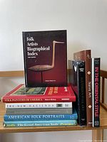Photo of nine American folk art books stacked and arranged standing, showing all titles and covers.