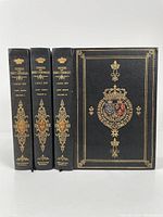 Front spines and cover of three leather-bound volumes with gilt and colored emblems.