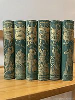Spine view of all six volumes showing gilt lettering and pictorial illustrations on green cloth covers.