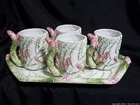 Four ceramic mugs and one rectangular platter with green leafy and pink floral motifs on a black background, showing overall set design.