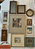 Overview of the 12 small art pieces including framed photographic prints, mirrors, a ceramic plaque, inlaid wood art, pressed flower art, and travel souvenirs, arranged on a white fabric surface.