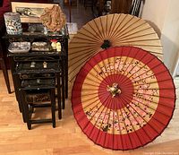 Photo showing four black stacking tables with removable glass tops, various chips visible, two paper parasols (red and tan) leaning against wall, and assorted small decorative items on tables.