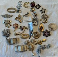 Wide shot showing the entire collection of vintage costume jewelry pins and brooches laid out on white fabric background.