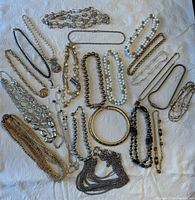 Photo showing variety of 19 costume jewelry necklaces laid out on white fabric background, displaying different colors, bead types, chains, and styles.