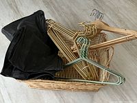 Basket with wood hangers, green and gold metal hangers, and two black zip-up suit protectors inside.