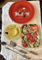 Florence Thomas red underplate, yellow divided bowl, Stokes apple tray, and three barbecue tools laid out on white cloth