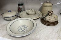 Photo of the full lot showing six pottery items: covered cheese set, canister, bowl, chip & dip, vase, and casserole dish