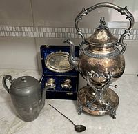Photo of all items in the lot showing the samovar, coffee pot, salt and pepper set in box, and swizzle spoon on marble countertop.