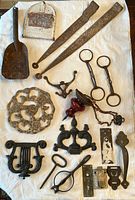 Full collection of rusty vintage metal hardware and decorative items laid out on white cloth: includes door hinges, horse bits, mailbox cover, boot scrape part, and assorted decorative metal pieces.