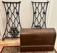 Pair of ornate black cast iron Singer sewing machine legs without wheels, and vintage bentwood Singer sewing machine case with metal handle and visible wear.