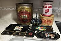 Photo showing the lot contents including 3 vintage tins and multiple decorated black metal trays with floral designs.