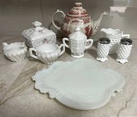 Image of the entire collection showing Victorian milk glass tray, Westmoreland candy dish, diamond cut cream and sugar set, Westmoreland covered sugar bowl, Fenton hobnail salt & pepper shakers and creamer, and contemporary red transfer ware teapot, all arranged on a surface.
