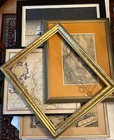 Photo showing a variety of framed wall art including vintage maps, a detailed sketch of a woman, and empty frames. Includes cracked glass on a gold ornate frame.