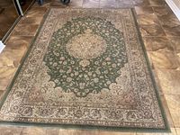 Full view of the rectangular area rug on tiled floor showing elaborate central medallion floral pattern with green and beige colors.