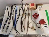 Full display of all bolo ties, money clip with large ring, square dancing necktie, travel alarm clock in box, and pocket magnifier.