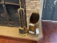 Brass fireplace tool stand with shovel, brush, poker, and tongs. Ash container with white porcelain handles nearby.