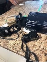 Two cameras on a stone countertop alongside their cases and original Panasonic box.