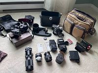 Photo showing various camera accessories including binoculars, lenses, flashes, cases, and cords arranged on the floor.