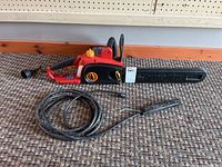Full side view of the red and black Homelite electric chainsaw with protective blade cover and coiled black extension cord with plug.