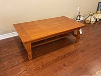 Front and angled view showing flat top surface and open lower shelf of oak mission style coffee table on hardwood floor.