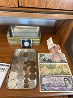 Photo showing Canadian 10 dollar note from 1954, Costa Rican 50 and 100 colones notes from 1992, Canadian 2 dollar note from 1986, assortment of coins, and a metallic container.