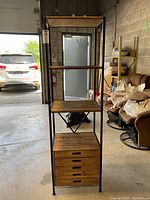 Full view of the display shelf showing black metal frame, three plywood shelves, and five drawers at the bottom.