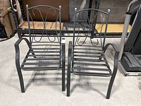Two black metal outdoor patio chairs with slatted seats and curved decorative backs, no cushions, minor wear visible.