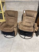 Matching pair of brown fabric glider chairs with padded armrests and tufted backs, placed on a concrete floor.