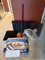 Overview photo showing lot components including box of Dr. Ho's Circulation Promoter, weighted lap blanket, wedge pillow, fan, heater, exercise bands, and a red cane.