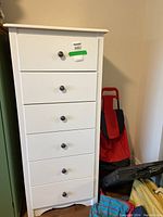 Front view of tall white highboy dresser with six drawers and round metal knobs.