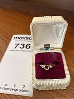 Ring inside vintage white textured ring box with maroon velvet insert, showing overall ring appearance and box condition.