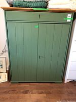 Front view of green painted cupboard with natural wood top and locked doors