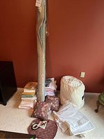 Lot of linens and textiles including folded sheets, pillows, rolled carpet, knit blanket in bag, all arranged on carpet flooring.