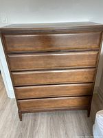 Front view of mid century modern highboy dresser with five drawers and walnut stain veneer.