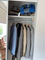 Closet view showing five jackets hanging on rod and folded wool sweaters on shelf above, including blue pinstripe suit jacket and jackets with herringbone and faux fur lapel details.